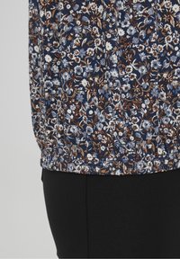 Haut fleuri bleu marine, orné de fleurs blanches et brunes, avec un ourlet froncé et une texture douce. Associé à un bas noir, offrant une coupe ajustée.