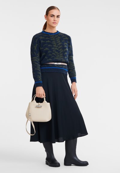 Navy sweater with green leaf pattern, blue accents; black skirt; black rubber boots; beige handbag with silver hardware.