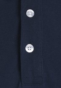 Mørkeblå polo shirt med struktureret stof, to runde hvide knapper og detaljer med broderet krave.