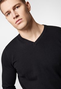 Czarny sweter w serek wykonany z gładkiego, dzianinowego materiału. Posiada subtelny żebrowany dekolt i dopasowany krój.