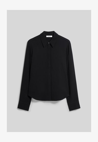 Chemise noire à manches longues avec col, boutons dissimulés et poignets droits, présentée sur un fond gris clair uni.