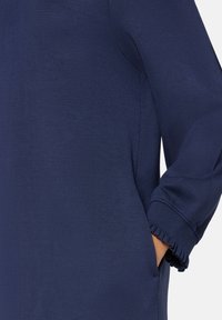 Marineblauer Pullover mit glatter Textur, versehen mit gerippten Bündchen, seitlichen Taschen und einem lockeren Schnitt. Einfaches, minimalistisches Design.