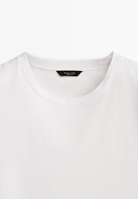 T-shirt blanc uni à col rond avec une étiquette noire cousue à l'intérieur du col.