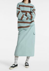 Maglione a righe azzurro chiaro con dettagli marroni, abbinato a una gonna midi verde menta chiara con tasche laterali e scarpe nere con suole bianche.
