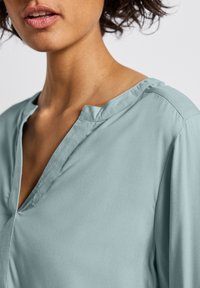 Blouse bleu clair avec un décolleté en V, texture douce et design décontracté. Dispose d'un col et de détails de couture subtils.