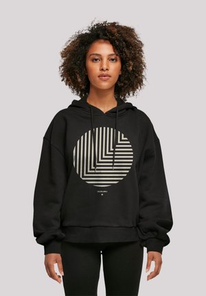 Black hoodie featuring a large circle graphic with alternating striped patterns in beige. Constructed from soft fabric, it has a loose fit and drawstrings.