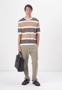 Maglione lavorato a maglia con righe orizzontali marroni e crema, abbinato a pantaloni verde oliva e borsa tote in pelle nera. Sandali completano il look.