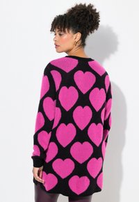 Übergroßer schwarzer Pullover mit großen rosa Herzmustern, aus einem weichen, strukturierten Material, mit schwarzen Rippbündchen und -saum.