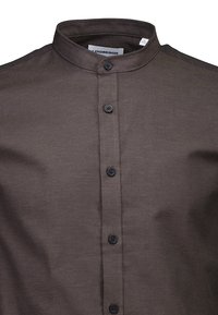 Camicia marrone con colletto in cotone, caratterizzata da una patta con bottoni scuri, dalla texture liscia e dal design minimalista.