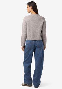 Pull gri deschis, texturat, cu guler rotund și mâneci lungi, asortat cu blugi albaștri lejeri și adidași cenușii casual.