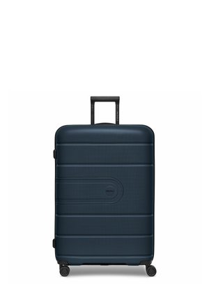 Valise rigide bleu foncé avec une surface texturée, des rainures horizontales, une poignée rétractable et quatre roues pivotantes noires.