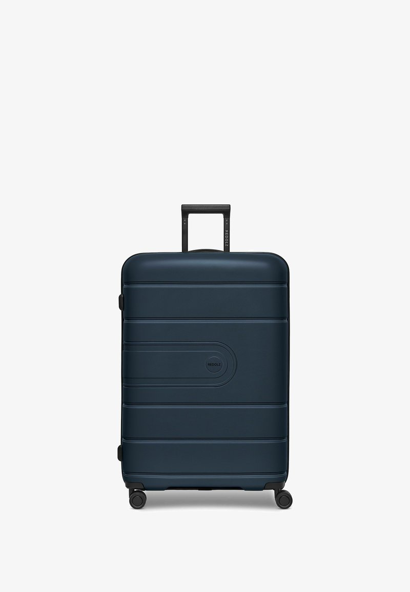 Valigia rigida di colore blu scuro con superficie texturizzata, scanalature orizzontali, manico telescopico e quattro ruote girevoli nere.