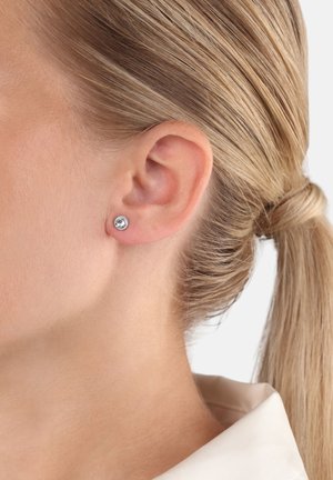 Silberne Steckerohrringe mit einem klaren Edelstein, rundem Design und polierter Oberfläche, getragen am Ohr eines Modells, das Einfachheit und Eleganz ausstrahlt.