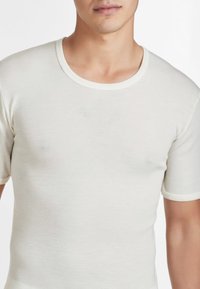 T-shirt a manica corta, collo rotondo, color bianco sporco, realizzato in morbido tessuto con bordature a contrasto attorno al collo e alle maniche. Texture liscia.