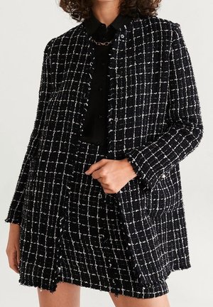 Zwart-witte tweed jas met een ruitpatroon, voorzien van een ronde halslijn, gestructureerde stof, drukknopen en zijzakken.