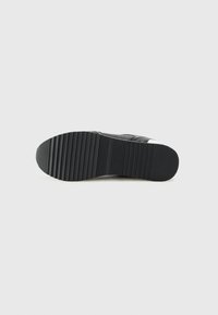 Semelle de sneaker noire avec une finition en caoutchouc texturé, présentant des rainures profondes et une forme arrondie pour une meilleure traction. Design minimaliste sans accents visibles.