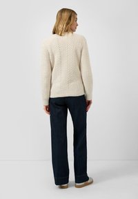 Cremfarbener Kabelstrickpullover mit strukturiertem Design, kombiniert mit dunkelblauen weiten Jeans. Lässige Passform mit gerippten Bündchen und Saum.