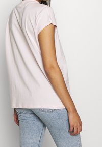 Ljust rosa bomullströja med korta ärmar, avslappnad passform och rundad halsringning, kombinerad med ljusblå denimjeans.