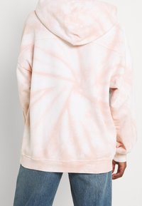 Hoodie v jemném lososovém tie-dye vzoru. Disponuje měkkou, texturovanou tkaninou, volným střihem a žebrovanými manžetami na rukávech a na spodním lemu.