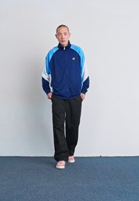 Jacket azul marinho e claro com fecho éclair, acentuado com branco, combinado com calças pretas e ténis cor-de-rosa. Tecido suave com um corte descontraído.