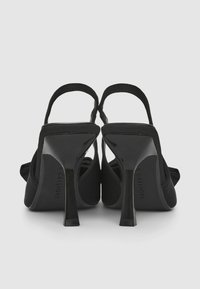 Schwarze High Heels Sandalen mit elegantem Design, spitzem Zehenbereich, aus Stoffmaterial und verstellbarem Knöchelriemen. Sie verfügen über einen glänzenden Absatz und eine subtile Textur.