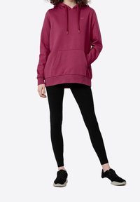 Felpa bordeaux con tasca a marsupio, cappuccio con lacci e dettaglio del logo, abbinata a leggings neri e scarpe da ginnastica nere.