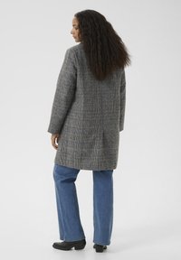 Grau karierten Langmantel aus strukturiertem Stoff, mit geradem Schnitt, einem Schlitzausschnitt hinten und lässigen blauen Jeans.