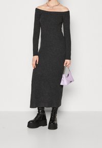 Schulterfreies, langärmeliges, dunkelgraues Strickkleid mit schmaler Passform. Kombiniert mit schwarzen Plateau-Stiefeln und einer kleinen Lavendel-Handtasche.