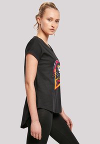 Svart t-skjorte med korte ermer og grafisk trykk av en kvinne, fargerike detaljer og en løs passform. Kombinert med svarte leggings.
