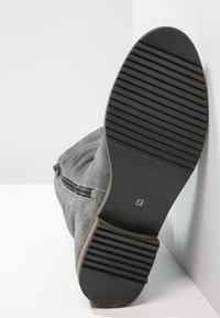 Bottines en suede grises avec une semelle en caoutchouc noir texturé, détail de fermeture éclair sur le côté, et étiquette de taille 37 visible sur la semelle.