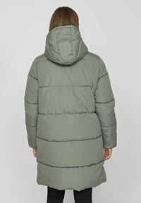 Parka verde esponjosa con capucha, que presenta secciones horizontales cosidas, mangas largas y un diseño de largo hasta medio muslo. Textura suave.