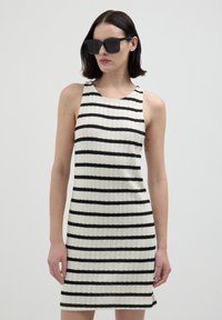 Gestreiftes ärmelloses Kleid aus einem Strickstoff, mit schwarzen Streifen auf weißem Hintergrund, in taillierter Silhouette und rundem Ausschnitt.