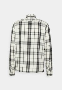 Flanellskjorta, svart och vit rutmönster, långa ärmar, knäppta manschetter och vanlig krage. Mjuk tyg med synliga sömdetaljer.