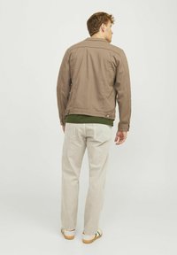 Chaqueta de lienzo marrón con cuello, combinada con una blusa verde y jeans beige claros. El conjunto presenta un corte holgado y un estilo casual.