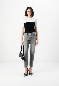 Black and white cropped top, gray jeans, black handbag, and glossy black heels. Model stands against a plain light backdrop.