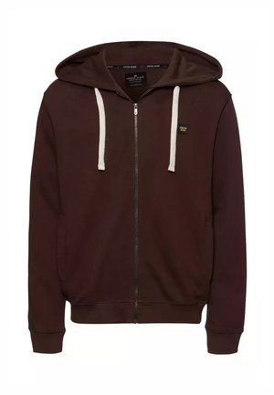 Brązowa hoodie na zamek błyskawiczny z białymi sznurowadłami, kieszeniami z przodu i ściągaczami przy mankietach. Posiada małe logo po lewej stronie klatki piersiowej. Miękka tekstura materiału.