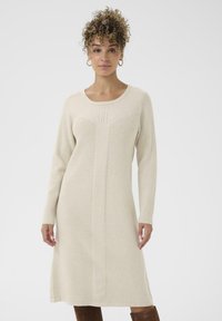 Hosszú ujjú kötött ruha krémszínben, kerek nyakkivágással, texturált mintázattal és enyhén bővülő szegéllyel. Simaságát a bordás anyag adja.