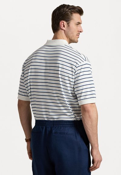 Camisola polo branca com riscas horizontais azuis, mangas curtas e colarinho canelado. Acompanhada de calções elásticos azuis-marinho.