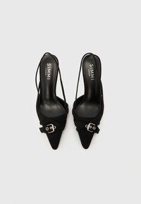 Melnas zamšādas augstpapēžu kurpes ar slīpi uz aizmuguri vērstu siksniņu, smailiem purngaliem, sakrustotām siksnām un dekoratīvu sudraba sprādzi priekšējā siksnā.