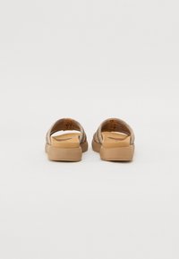 Sandales beige métalliques avec un dos ouvert, dotées de sangles texturées et d'une semelle beige lisse et plate.