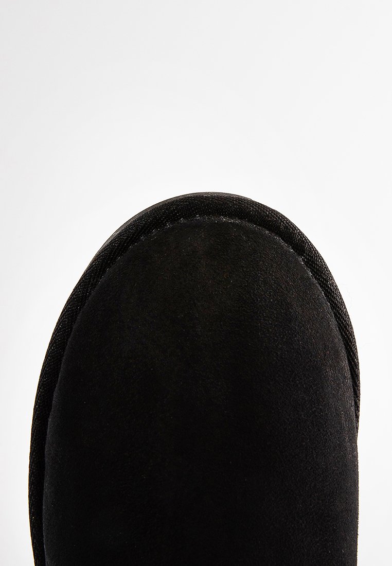 Bottine en daim noir avec un bout arrondi et un bord piqué. Texture douce avec une finition lisse et une tige flexible, adaptée pour un usage décontracté.