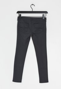 Slim-fit zwarte jeans hangen aan een hanger. Kenmerken zijn een gladde textuur, twee achterzakken met decoratieve stiksel en een middelhoge taille.