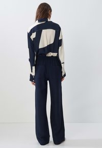 Navy and cream patterned blouse with long sleeves paired with navy wide-leg pants, featuring an elastic waistband and pockets.