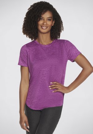 Short-sleeve purple athletic shirt with a textured finish, rounded neckline, and a slightly curved hem. Model wears black leggings.