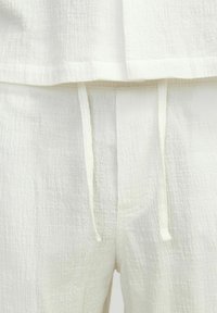 Hvidt tekstureret loungewear sæt med en boxy top og en afslutning samt bukser med snoretræk. Blødt, let stof med subtilt rutenetmønster.