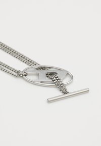 Colier argintiu cu un lanț dublu, având un pandantiv oval și un închizător tip bară. Textură metalică netedă cu un design de lanț împletit.