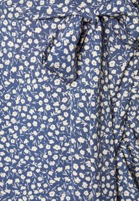 Tissu floral en bleu avec des fleurs blanches et des tiges vertes. Le matériau est léger avec une texture douce, présentant un détail de nœud noué.