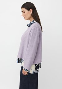 Lavendelstickad tröja med långa ärmar, boxig form och en texturerad finish, lager på lager över en mönstrad blus med en marinblå krage.