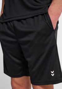 Zwarte sportieve shorts van soepel stof. Voorzien van voorzakken, een elastische tailleband en een klein lichtroze logo aan de zijkant.