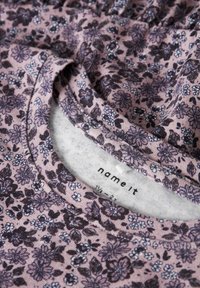 Tissu à motif floral dans des nuances de rose et de violet foncé, avec un col rond et une doublure intérieure douce. Étiquette de la marque visible à l'intérieur.